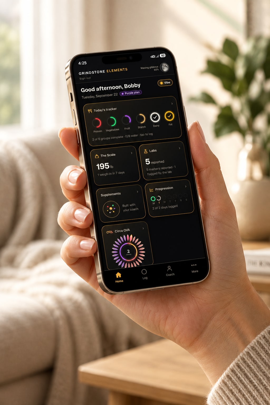 A hand holding a phone showing the Grindstone Elements home screen: today's tracker, the scale, labs, supplements, progression and Circa OVA